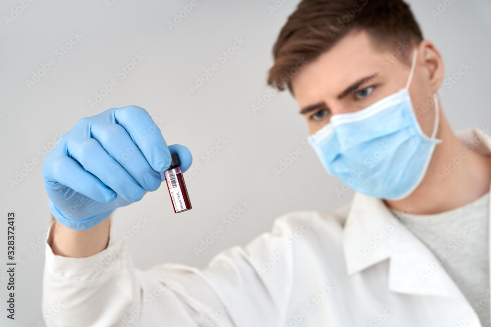 Doctor in protective workwear and face mask looking at blood sample Doctor in protective workwear and face mask looking at blood sample