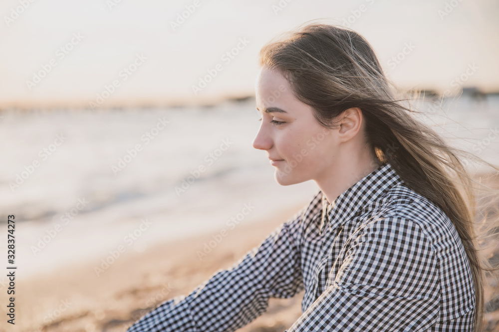 a pretty girl in a plaid dress and jacket sits on the sandy beach at sunset a pretty girl in a plaid dress and jacket sits on the sandy beach at sunset
