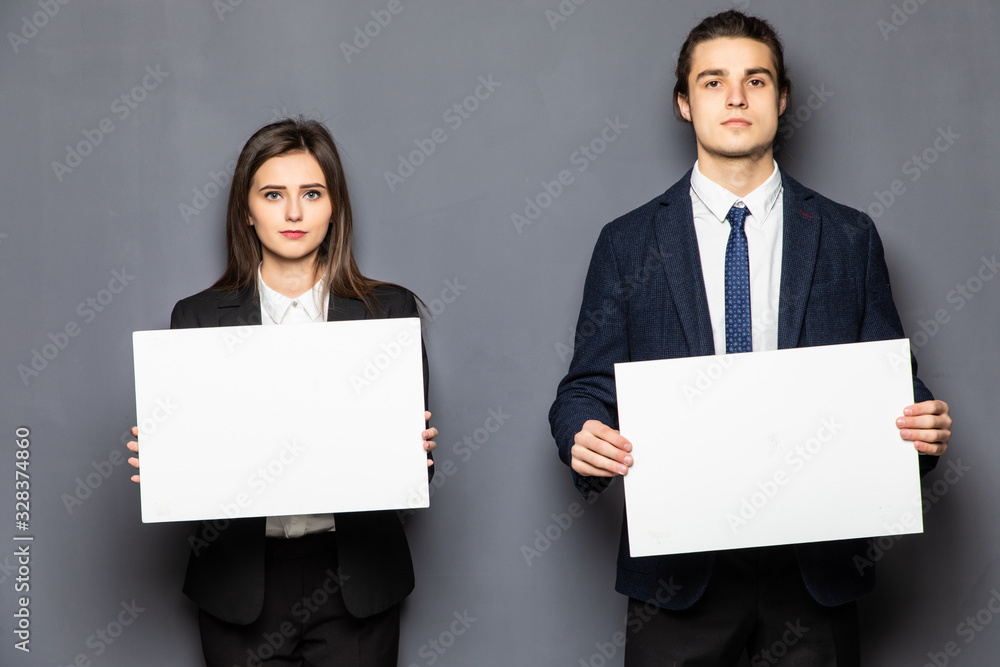 Confident business couple standing with blank board to advertise or invite isolated on gray background Confident business couple standing with blank board to advertise or invite isolated on gray background