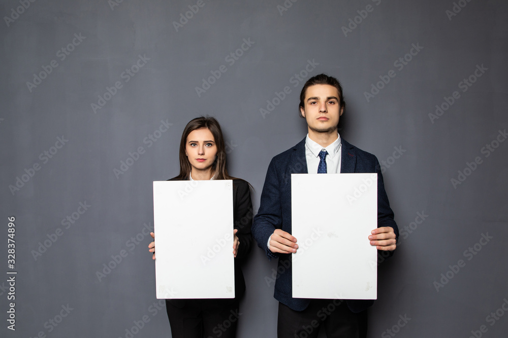 Confident business couple standing with blank board to advertise or invite isolated on gray background Confident business couple standing with blank board to advertise or invite isolated on gray background