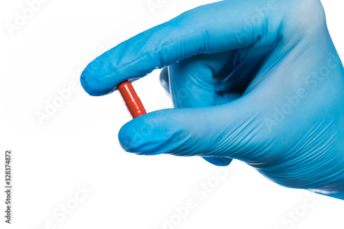 Surgeon's hand in a blue medical glove holds a pill blister isolated on white background