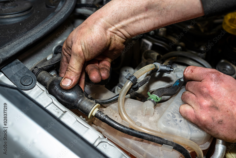 The mechanic bleeds the fuel system with a pump that is on the fuel line, after installing a new fuel filter, the man's hands are visible.