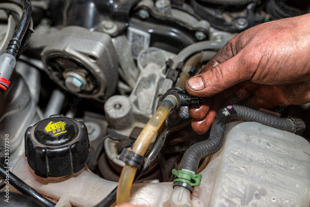 The mechanic bleeds the fuel system with a pump that is on the fuel line, after installing a new fuel filter, the man's hands are visible.