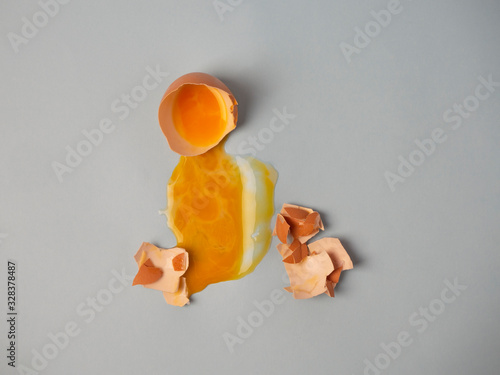 Broken raw brown egg, a yellow yolk leaked and spread on the area, a smitten shell nearby isolated on a blue background top view.