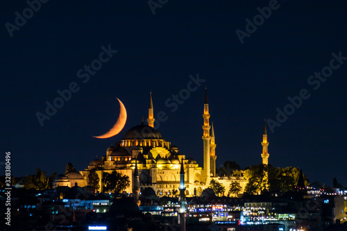 The moon stands like a crescent moon over the Fatih Mosque at night
