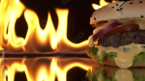 An appetizing burger with a with meat, tomato, onion and salad close-up, a fire blazes in the background.