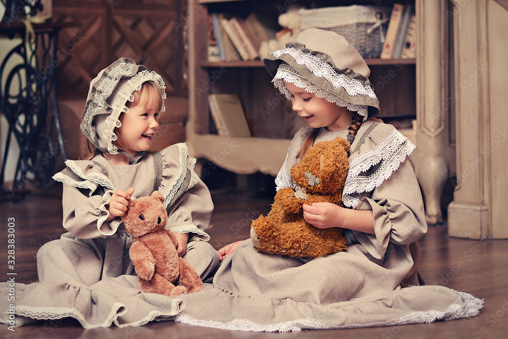 Two happy little sisters in retro outfits play with teddy bear . Retro style.