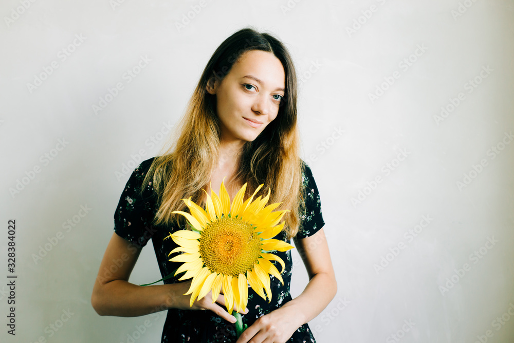 a young pretty girl in a black floral dress holds a vase of sunflower flowers on a white background a young pretty girl in a black floral dress holds a vase of sunflower flowers on a white background
