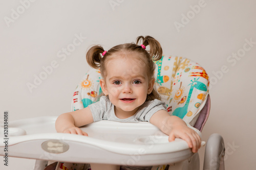baby girl sitting in a child's chair eating fruit on a white background. baby food concept, space for text