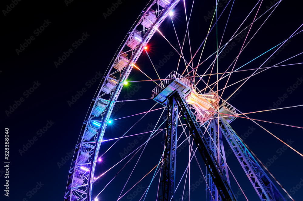 Amusement park at night - big ferris wheel with festive colorful illumination against blue evening sky