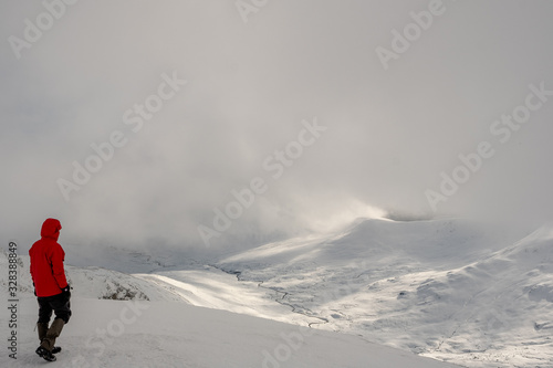 Man in red coat looking down a snowy mountain