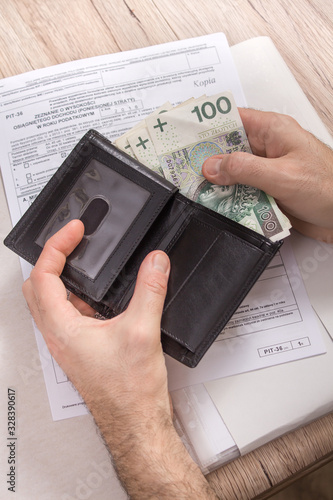 Obraz na płótnie Dłonie mężczyzny trzymają portfel z którego wyjmują banknoty PLN. Deklaracja podatkowa leży na drugim planie na blacie. w salonie
