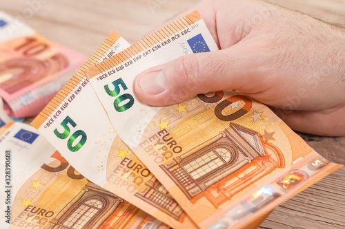 Obraz na płótnie Męska dłoń trzyma dwa banknoty o nominale 50 Euro. Na drugim planie banknoty euro leżą na stole. w salonie