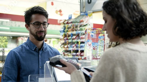 Smiling man paying with credit card in store. Bearded man in eyeglasses giving credit card to cashier and using payment terminal at cash register in supermarket. Shopping concept 