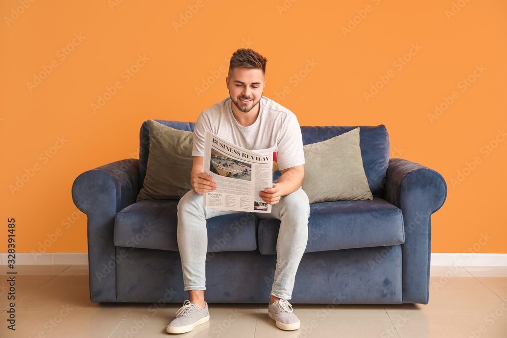 Young man reading newspaper while sitting on sofa at home Young man reading newspaper while sitting on sofa at home