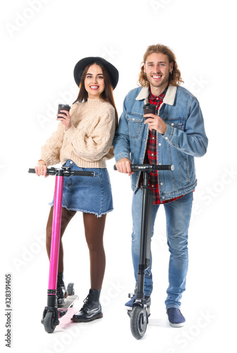 Young couple with kick scooters and cups of coffee on white background