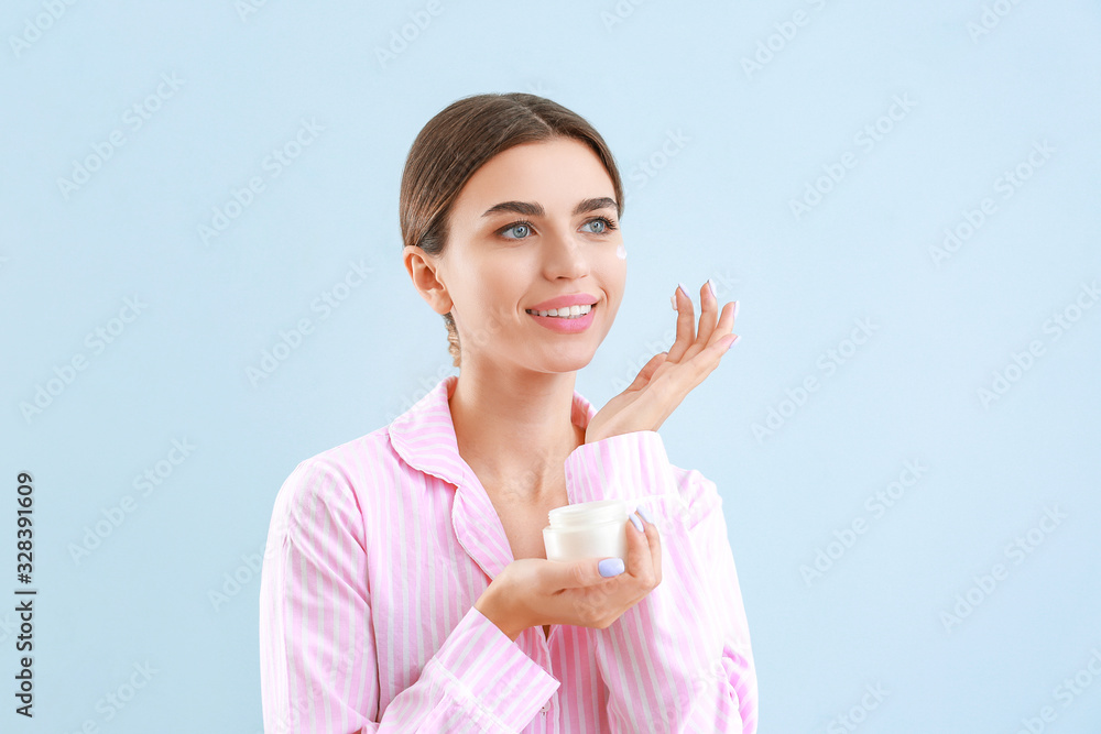 Beautiful young woman applying cream on her face against color background Beautiful young woman applying cream on her face against color background