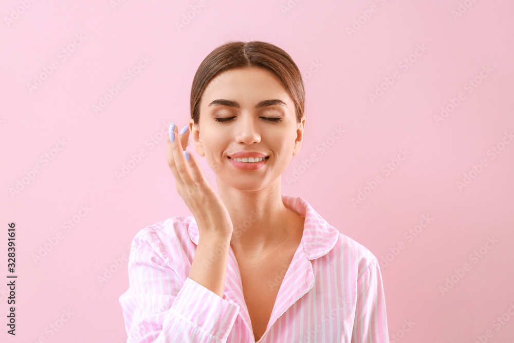 Beautiful young woman applying cream on her face against color background Beautiful young woman applying cream on her face against color background