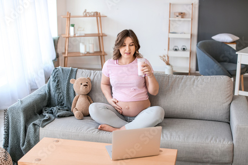 Beautiful pregnant woman with laptop resting at home