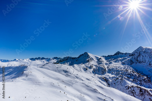 Beautiful mountain range covered in snow with clear sky, lens flare and sun star. Ski infrastructure and slopes in Pyrenees, Andorra © Dawid