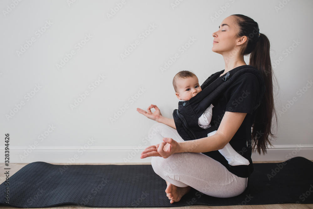 Young mother doing yoga with baby in ergo backpack Young mother doing yoga with baby in ergo backpack
