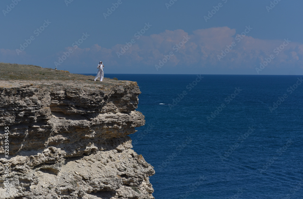 a girl in white clothes stands on the edge of a cliff above the sea a girl in white clothes stands on the edge of a cliff above the sea