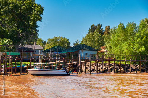 Tigra delta in Argentina, river system of the Parana Delta North from capital Buenos Aires. Lush vegetation, wooden houses. Motor boat by pier. Orange clay water of Lujan River delta system photo