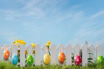 Spring grass and wooden fence with easter eggs and flower on cloudy sky