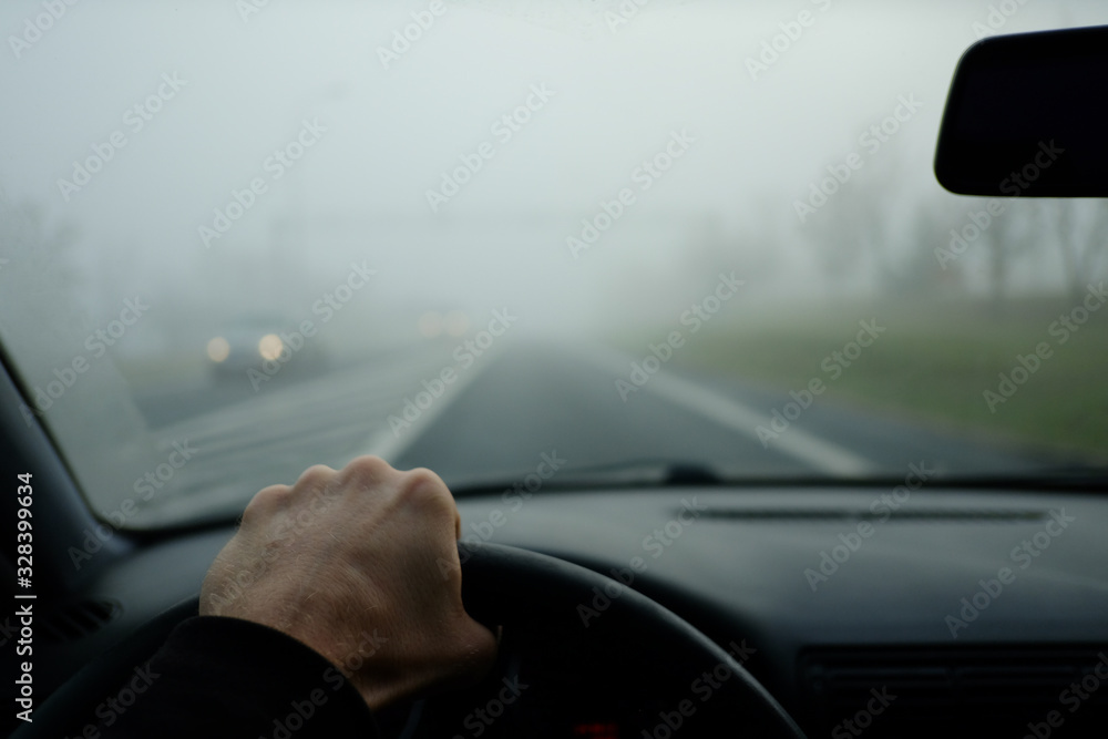 The road in the fog. The drivers hand holds the steering wheel. The meeting goes a car with lights included The road in the fog. The drivers hand holds the steering wheel. The meeting goes a car with lights included