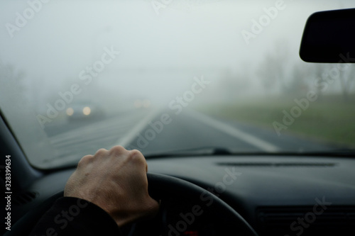 The road in the fog. The drivers hand holds the steering wheel. The meeting goes a car with lights included