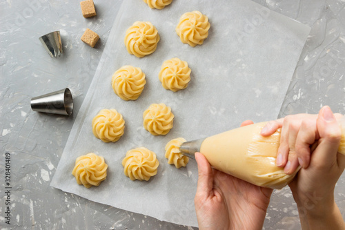 Cooking profiteroles, female hands  squeeze  the dough from the bag onto parchment, for baking.