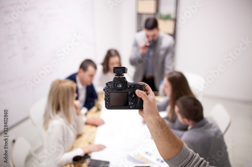 Photographing creatime meeting of young successful business people. Abstract hand holding prefessional dslr camera with wireless triger photo