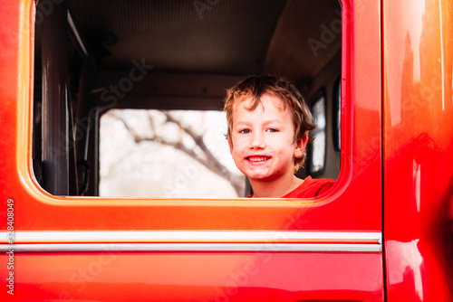Portrait of a boy with a really dirty face, smiling from inside a red car.