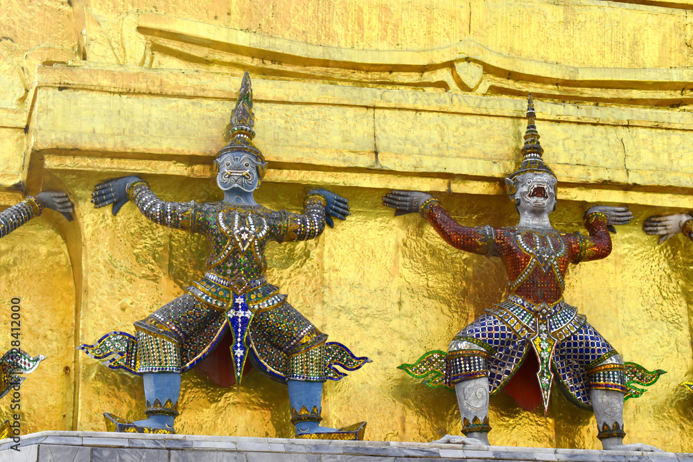 Demon guardian giant statues stand around pagoda and liftting the base of the golden pagoda at Wat Phra Kaew, Bangkok, Thailand.