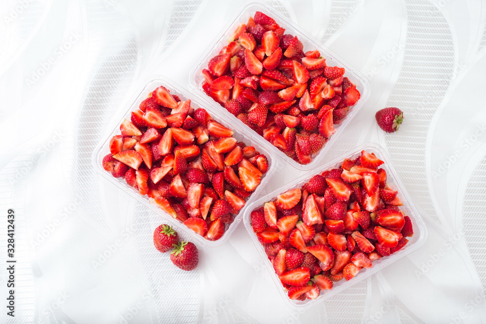 Sliced pieces of strawberries in transparent containers on a white background, top view