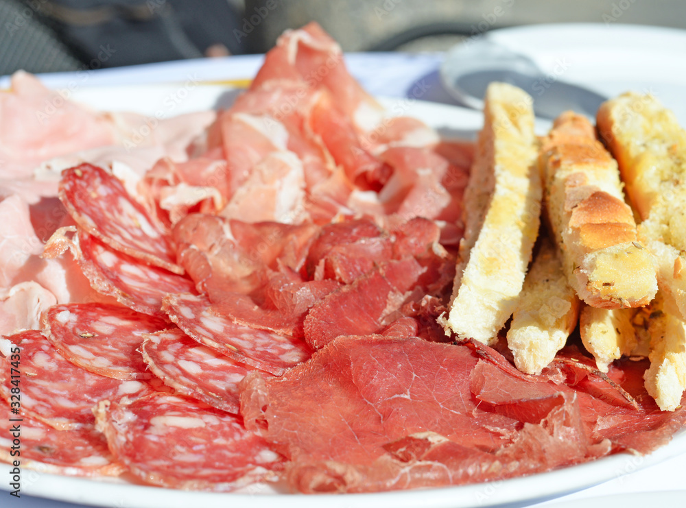 Plate with salami, ham and different sorts of cold cuts with toasted Italian bread and dried herbs. Selective focus Plate with salami, ham and different sorts of cold cuts with toasted Italian bread and dried herbs. Selective focus