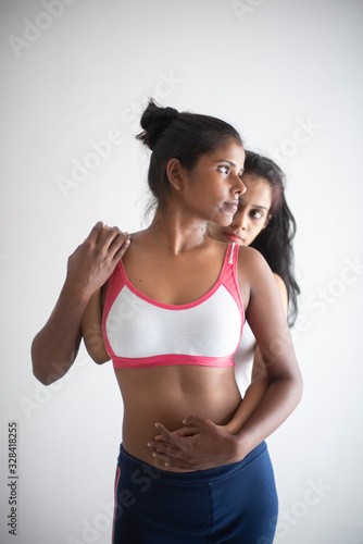 A beautiful and young Indian Bengali lesbian couple in sports inner/underwear are interacting in a intimate way in front of a white background. Dark and fare model, Indian lifestyle © abir