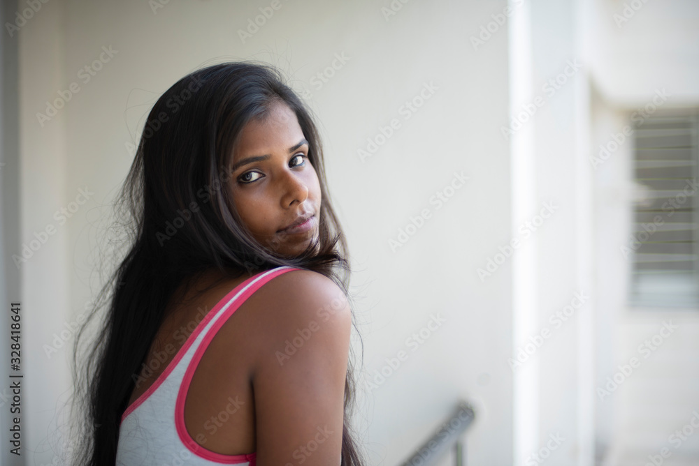 Portrait of an attractive young brunette dark skinned Indian Bengali girl in western sportswear standing on a balcony in white urban background. Indian lifestyle Portrait of an attractive young brunette dark skinned Indian Bengali girl in western sportswear standing on a balcony in white urban background. Indian lifestyle