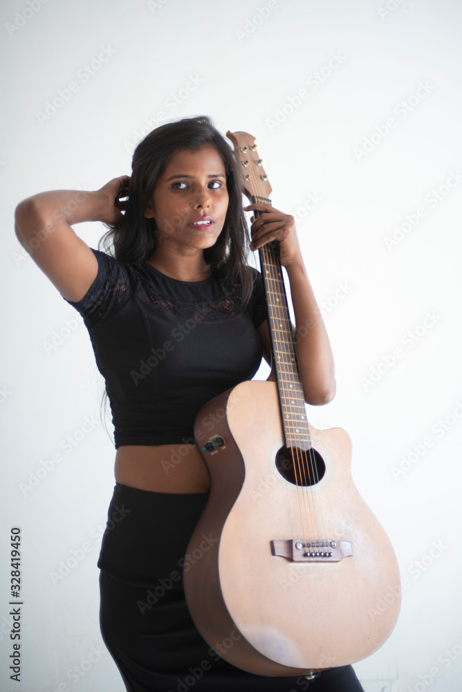 Portrait of an attractive young brunette dark skinned Indian Bengali girl in black western sportswear playing guitar in white studio background. Indian lifestyle Portrait of an attractive young brunette dark skinned Indian Bengali girl in black western sportswear playing guitar in white studio background. Indian lifestyle