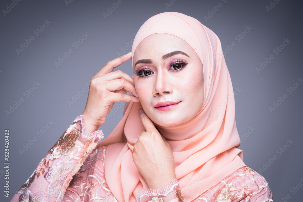 Headshot of a beautiful Muslim female model in an Asian Muslim traditional dress and hijab isolated on grey background. Eidul fitri fashion and lifestyle portrait concept Headshot of a beautiful Muslim female model in an Asian Muslim traditional dress and hijab isolated on grey background. Eidul fitri fashion and lifestyle portrait concept