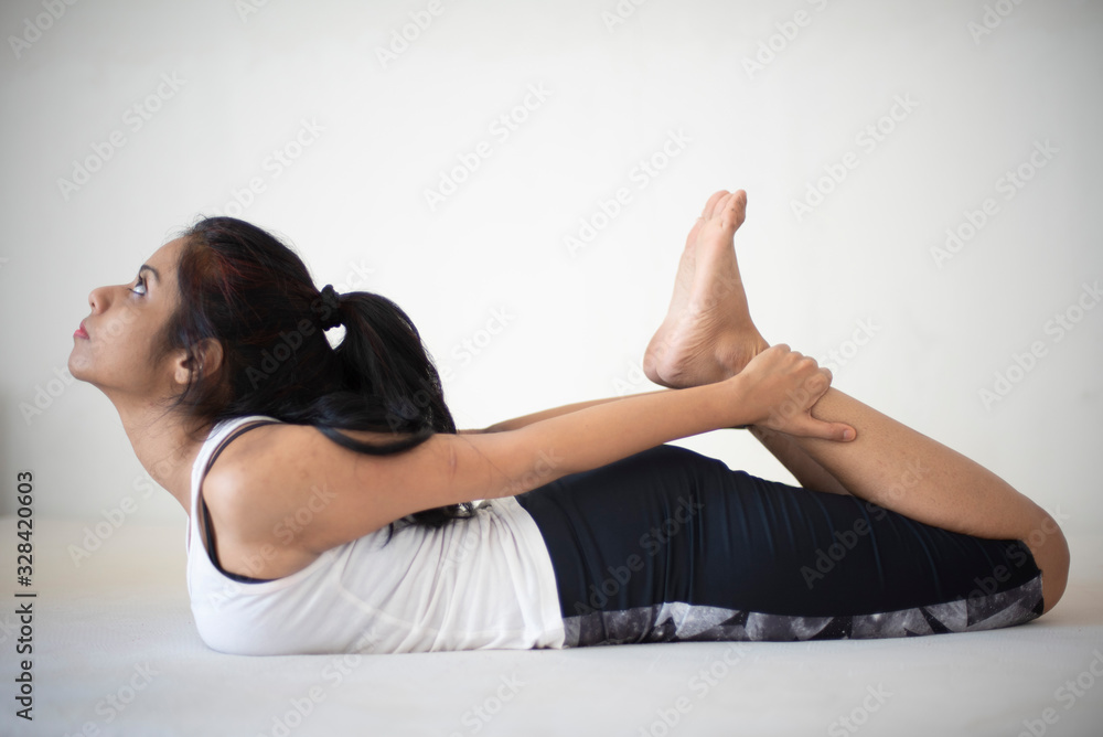 Obraz premium Indian brunette girl performing yoga/sports /exercise in sportswear in front of a white background. Indian lifestyle
