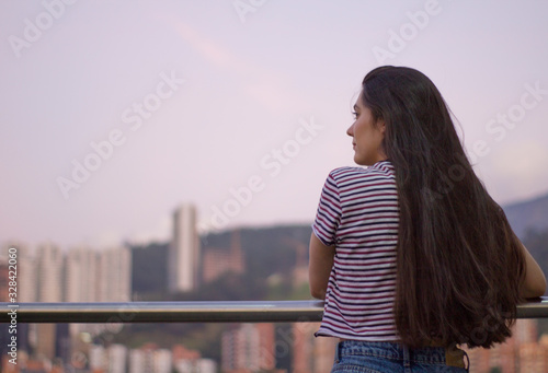 Chica mirando a un lado de la ciudad. Edificios y montañas al fondo. Medellin Colombia