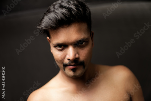 Face portrait of a confident muscular Indian brunette dark skinned macho man in bare body and underwear brief standing  in black  background. Indian lifestyle and fashion portrait
