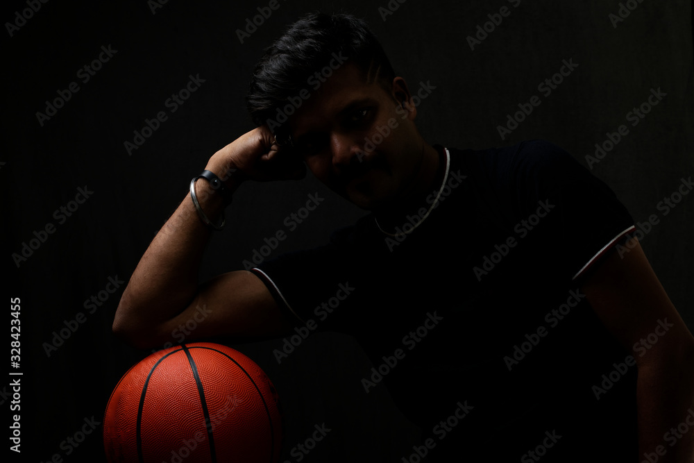Portrait of a handsome and intelligent Indian brunette man wearing a solid black t shirt standing before a copy space black background holding a basketball. Indian lifestyle and fashion portrait Portrait of a handsome and intelligent Indian brunette man wearing a solid black t shirt standing before a copy space black background holding a basketball. Indian lifestyle and fashion portrait