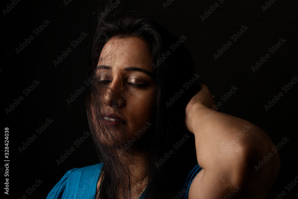 Close up face portrait of a beautiful Indian Bengali brunette woman in light and shadow before a black copy space background wearing a blue top. Indian lifestyle and fashion portrait Close up face portrait of a beautiful Indian Bengali brunette woman in light and shadow before a black copy space background wearing a blue top. Indian lifestyle and fashion portrait