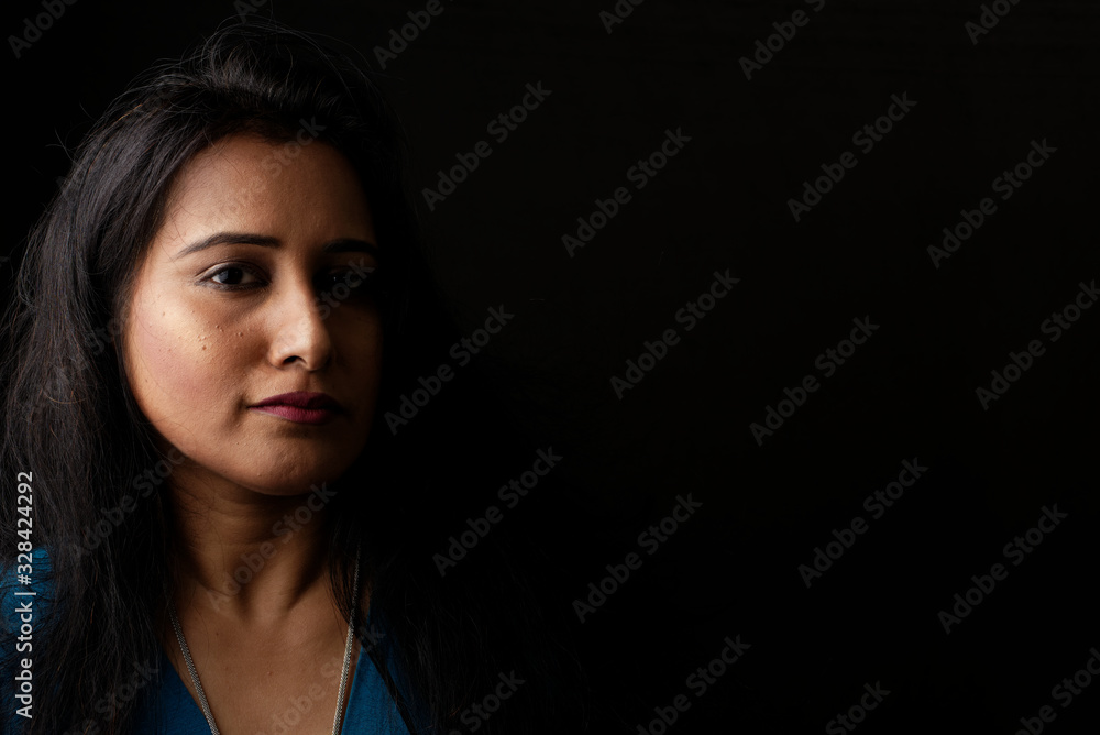 Φωτογραφία Close up face portrait of a beautiful Indian Bengali brunette woman in light and shadow before a black copy space background wearing a blue top