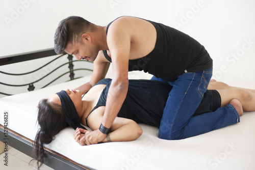 Attractive Indian Bengali brunette couple in black dress sharing intimate moments in white bedroom while the man is trying to put a sleep mask on the girl riding over her. Indian lifestyle 