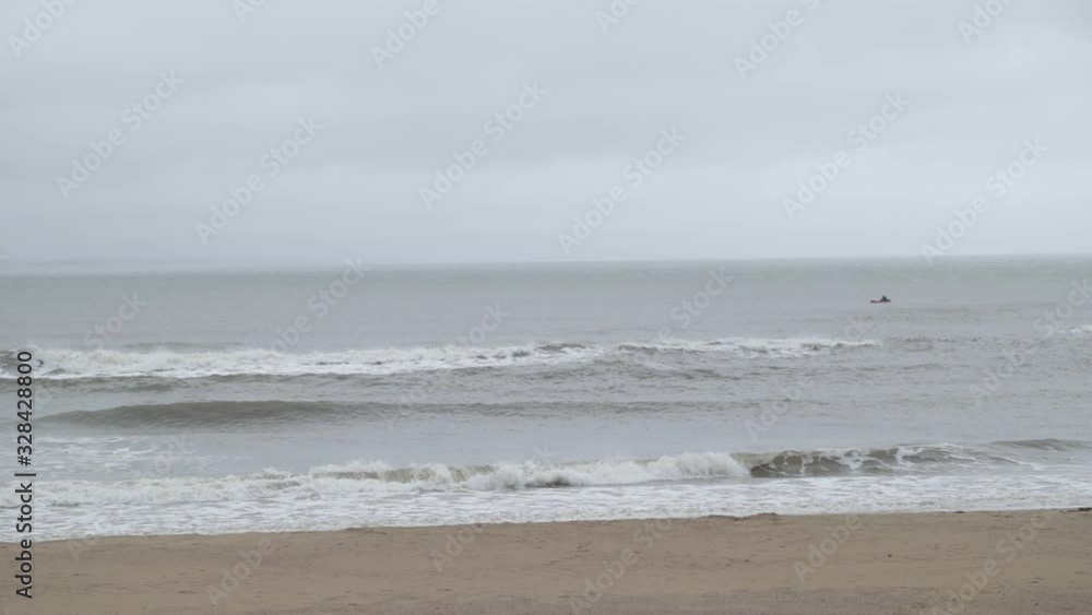 Slow motion of waves braking at sandy shore. Foam and splashing detail. Holiday spot at Jose Ignacio town, Rocha, Uruguay. Misty, cloudy day. Hills at background. Slow motion of waves braking at sandy shore. Foam and splashing detail. Holiday spot at Jose Ignacio town, Rocha, Uruguay. Misty, cloudy day. Hills at background.