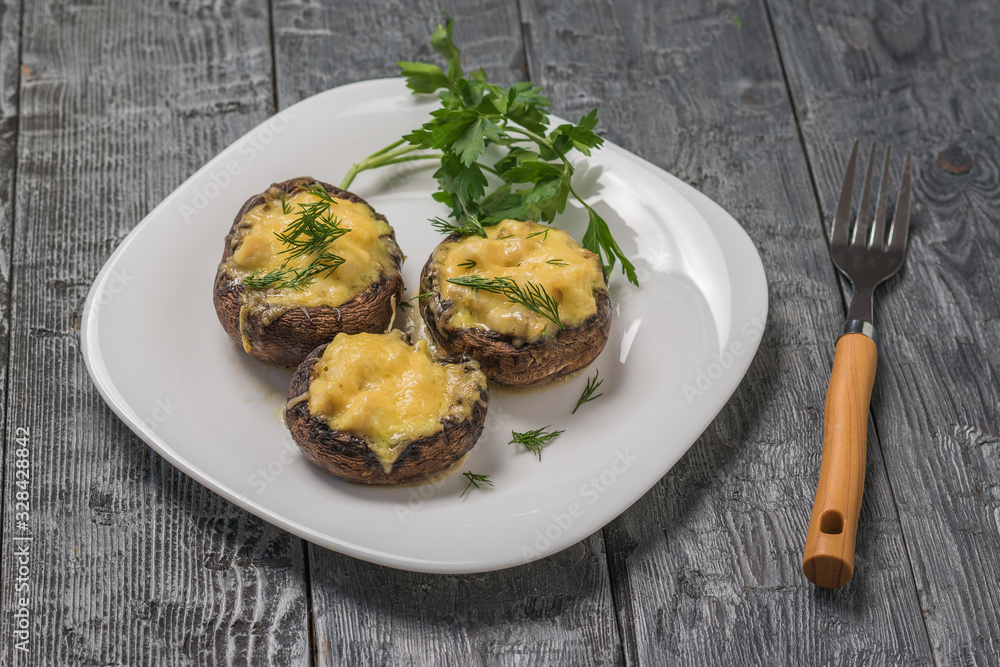Baked Royal mushrooms on a white plate and a fork with a wooden handle. Baked Royal mushrooms on a white plate and a fork with a wooden handle.