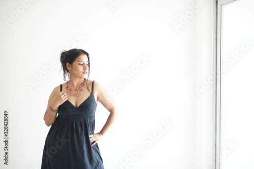 Fashion portrait of a beautiful Indian Bengali brunette woman wearing a black western dress standing in front of a white copy space background. Indian lifestyle and fashion portrait